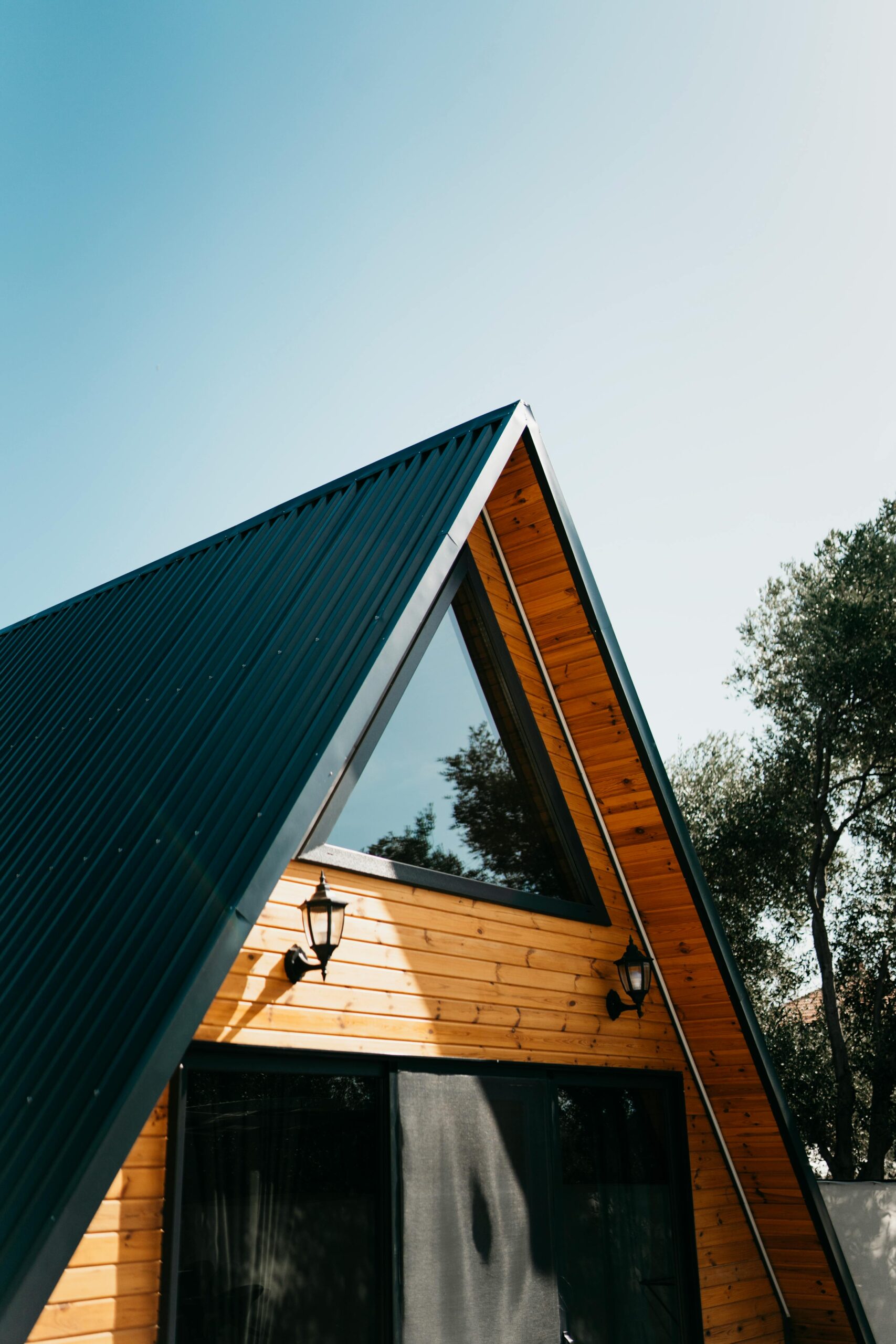 A modern A-frame wooden cabin with a sloping roof and large window, set in nature.